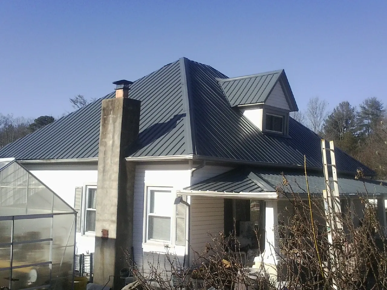 Dark blue standing seam metal roof on a white farmhouse with dormer — Slate & Tile Roof Repair by Roofing Brothers in Spring Lake