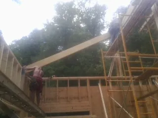 Carpenter raising a rafter beam on a new second story frame in Spring Lake