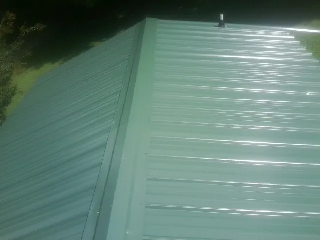 New green metal panels meeting at the ridge of a roof — Flat Roof Repair work by our crew in Spring Lake