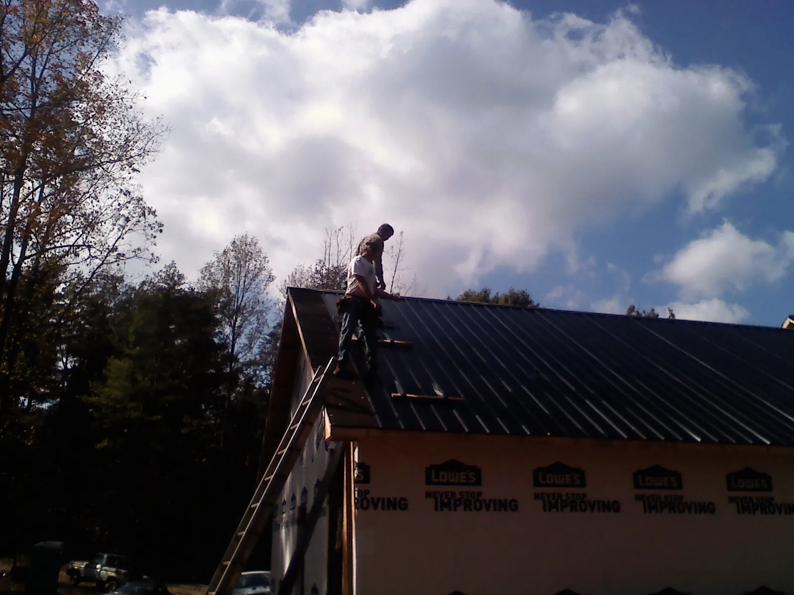 Roofer fastening dark metal panels high against a cloudy sky, from a Roof Inspection job in Spring Lake