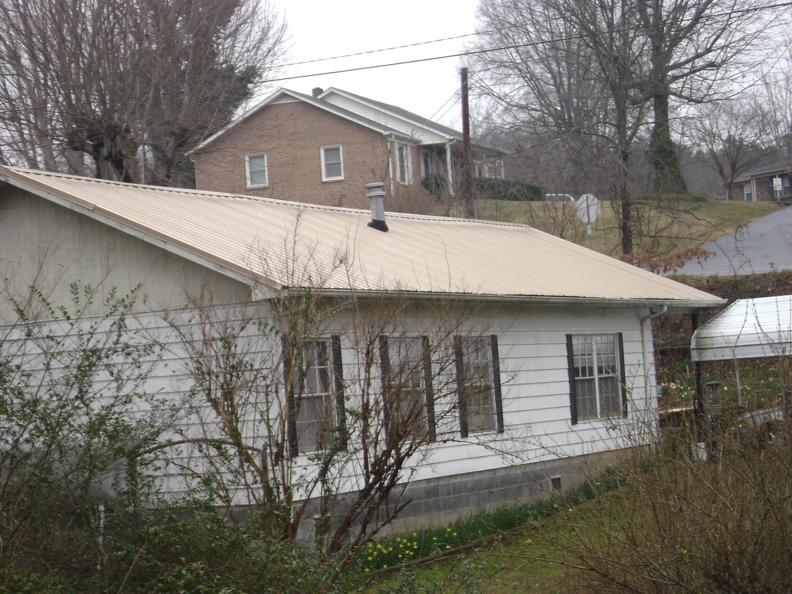 Tan metal roof on a white sided house set into a hillside — Commercial Roofing by Roofing Brothers in Spring Lake
